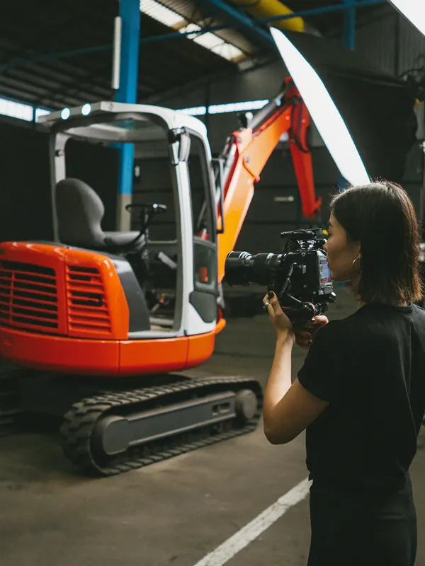 AI concept image: a videographer filming a new compact excavator in a lit studio