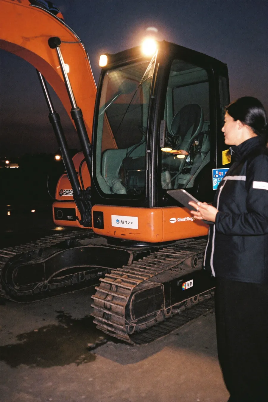 AI concept image: an export sales engineer with a tablet beside a new compact excavator in a factory yard at dusk