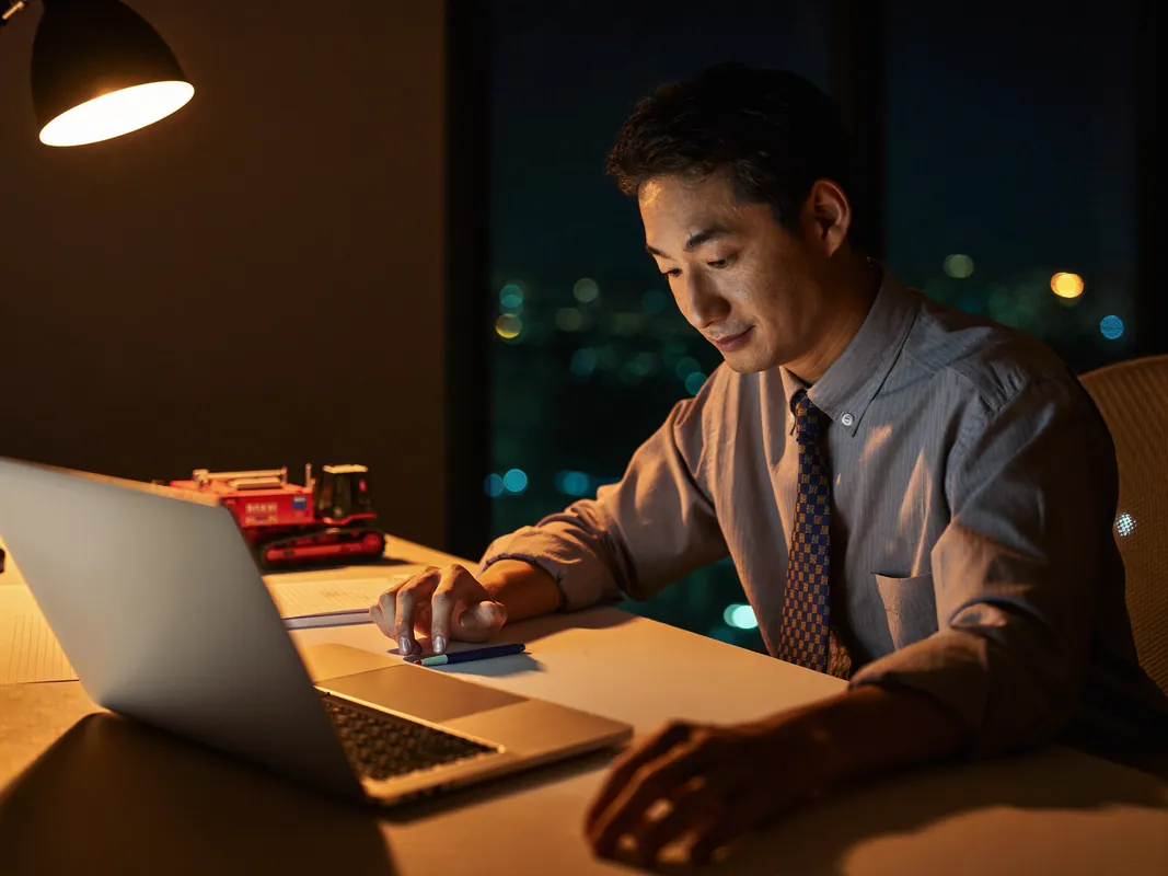 AI concept image: a sales researcher working late, a scale-model excavator on the desk